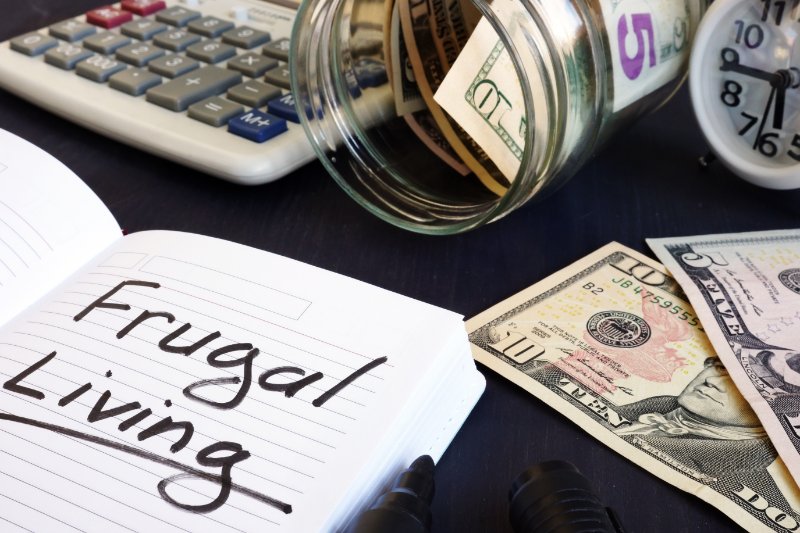 Frugal living written on a note pad and money.