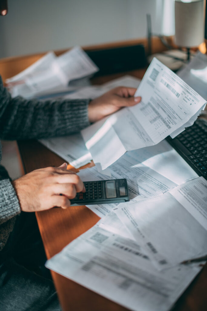 Close-up of a man's hands holding a utility bill, surrounded by checks and a calculator on a desk.