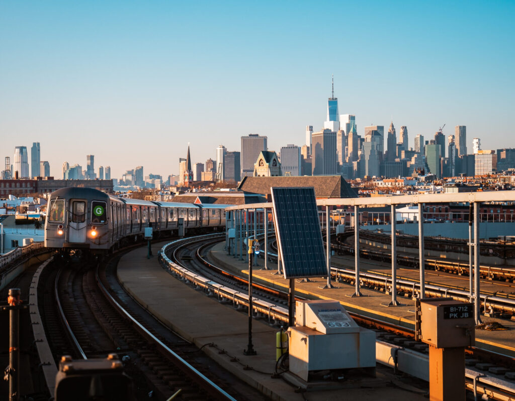 MTA train arriving at a metro station in Brooklyn, New York, with passengers waiting on the platform.