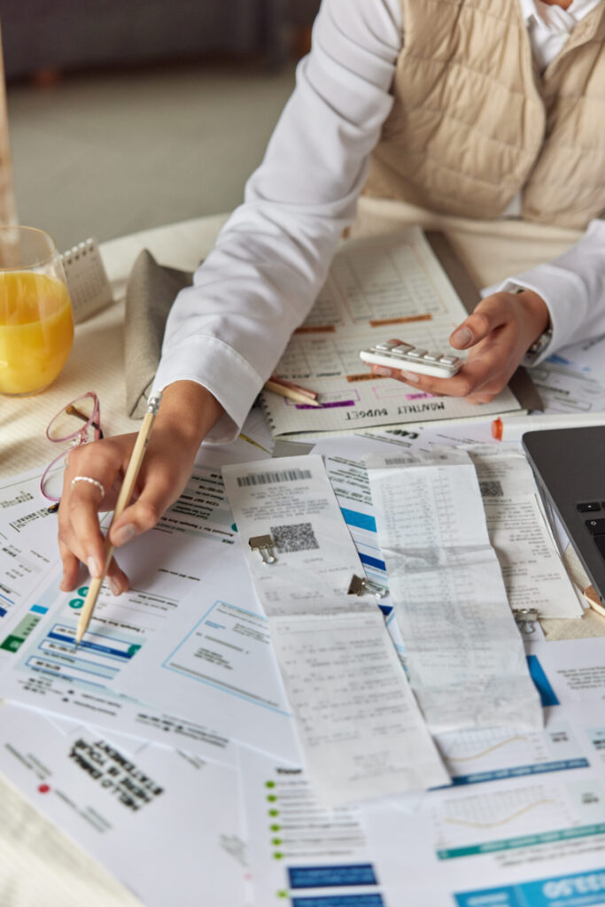 Woman managing family budget at home, reviewing bills and calculating expenses with a calculator in hand