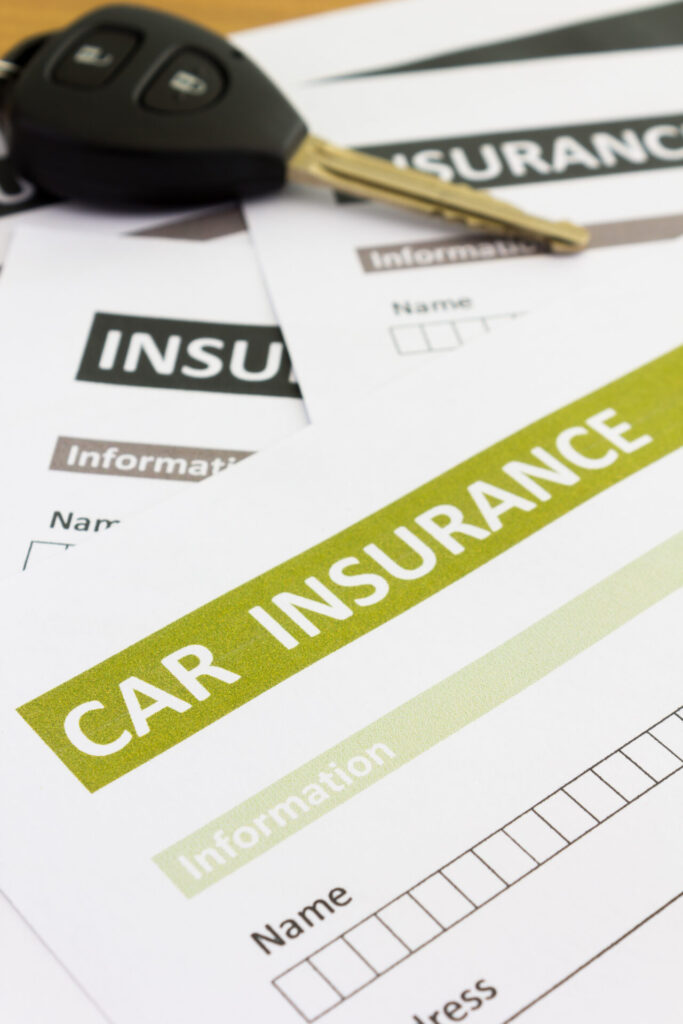 Car insurance forms alongside a set of car keys on a wooden surface, indicating preparation for vehicle coverage.