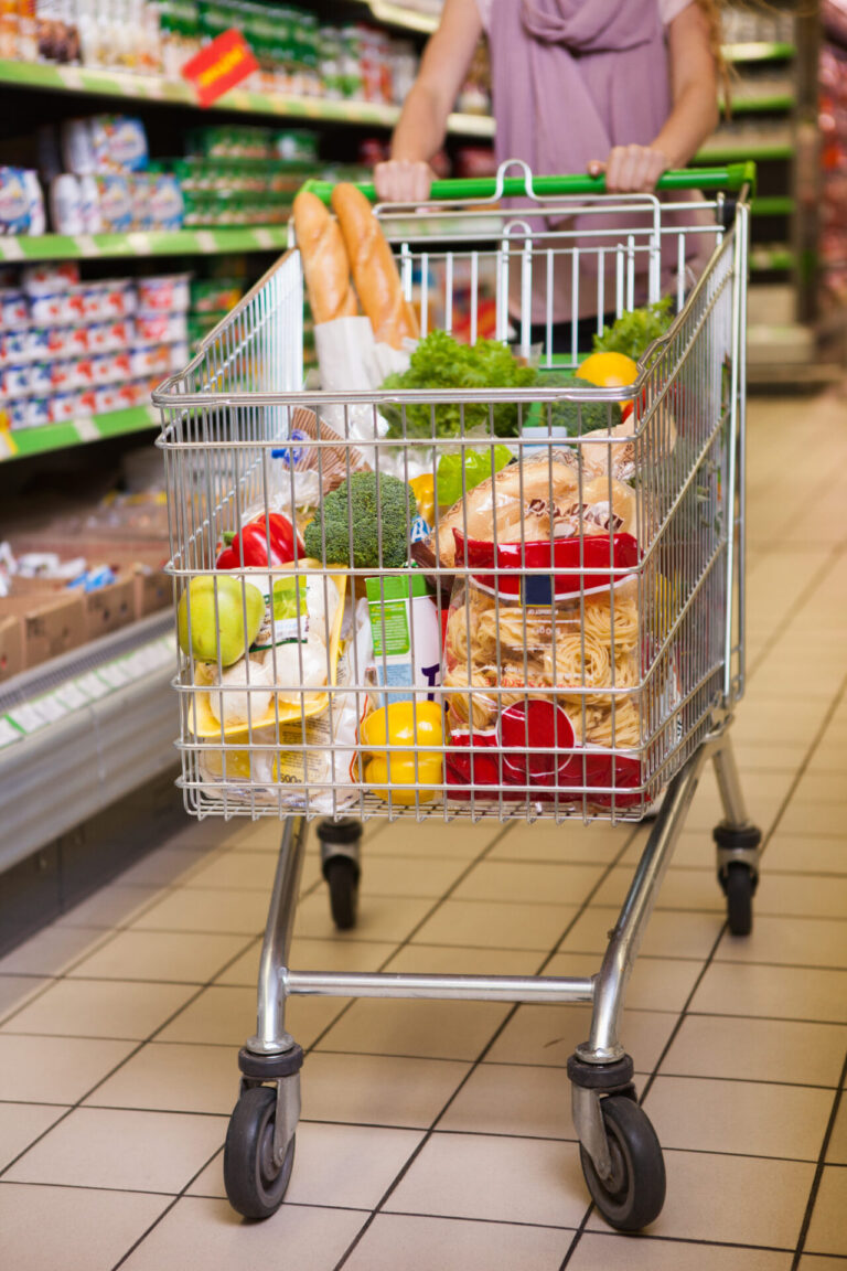 Shopping cart brimming with groceries, featuring fresh produce, canned goods, and household essentials.