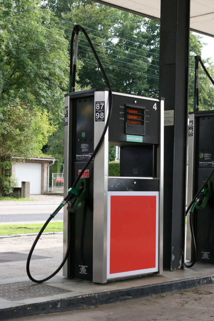 Exterior view of a gas station featuring several fuel pumps, a small shop, and a bright sign indicating fuel prices