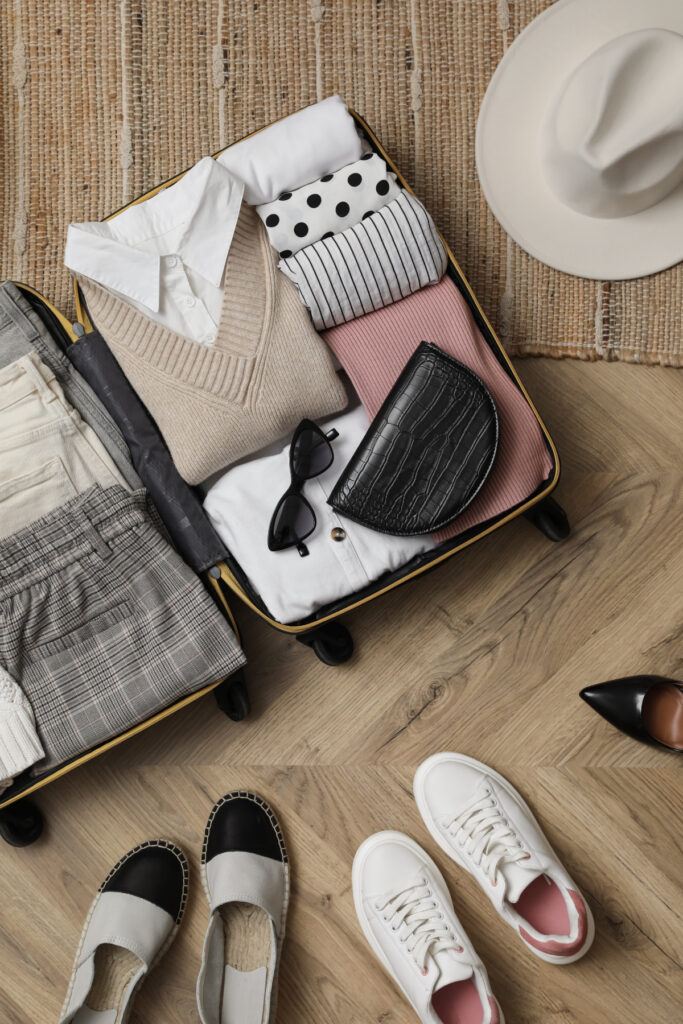 Flat lay of an open suitcase filled with folded clothes, shoes, and accessories placed on the floor for packing.
