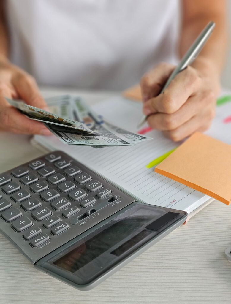 Person writing a home budget with a calculator, illustrating strategies for saving money on taxes.