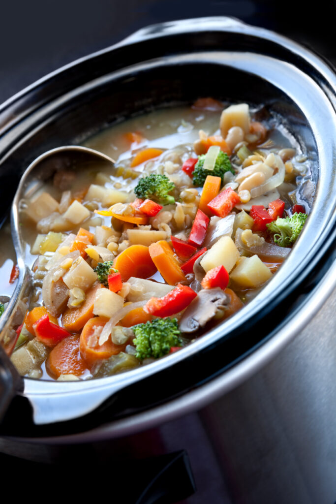 Close-up of a slow cooker filled with colorful, hearty vegetable soup, showcasing various vegetables simmering together.
