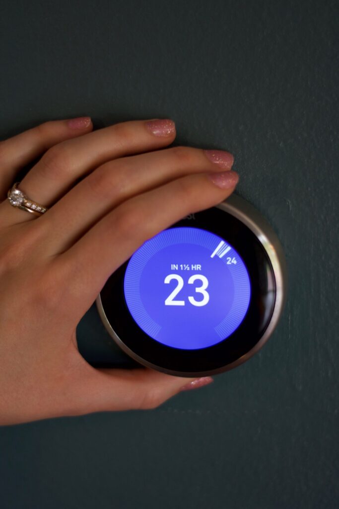 Hand of a woman modifies the temperature on a smart thermostat in Celsius against a blue wall