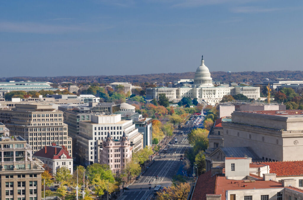 Washington D.C. skyline featuring Capitol Hill and prominent federal buildings against a clear blue sky.